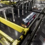 Industrial interior with a red and white tram on display. The space features high ceilings, large windows, and bright yellow overhead cranes.